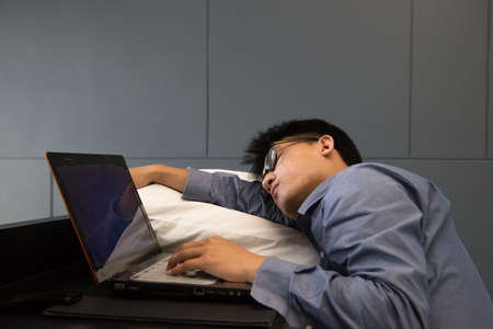 Tired asian businessman sleeping on a laptop with pillowの写真素材