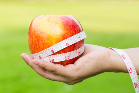Woman hand holding fresh apple with measuring tape