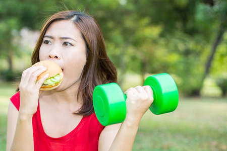 Asian woman eating hamburger with weight-lifting