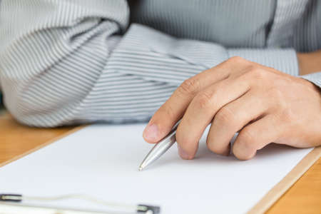 Human hand signing white paper on wood table