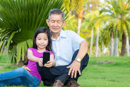 Asian grandfather and grandchild taking selfie with smartphone in the parkの写真素材