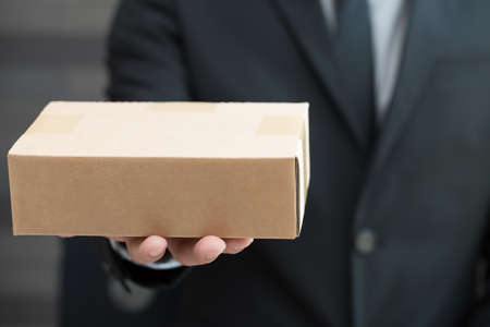Businessman in suit giving brown box to someoneの写真素材