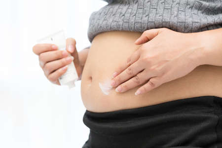 Pregnant woman applying cream on her bellyの写真素材
