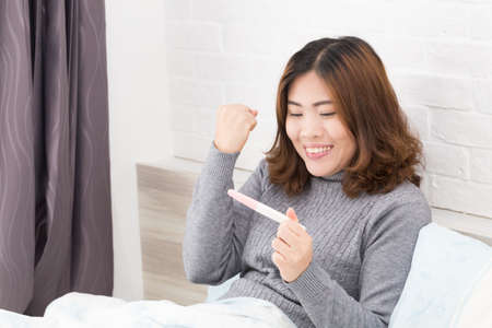 Happy asian woman holding pregnancy test and lying down in the bed, New life and new family concept.の写真素材