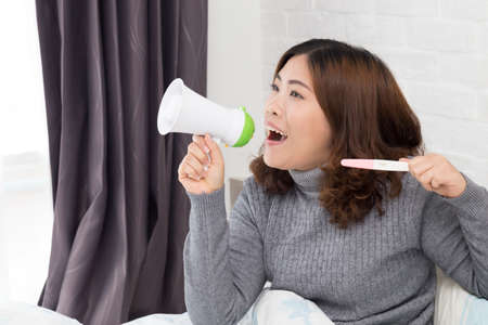 Happy asian woman holding megaphone and pregnancy test