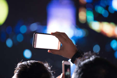 Hand with a smartphone records luxury party with blank white screenの写真素材