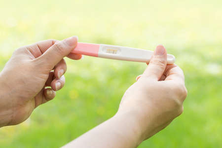 Woman holding pregnancy test in the green garden