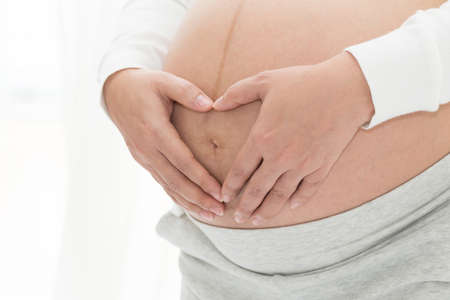 Close up of pregnant belly with hugging the tummy and hands in heart shape
