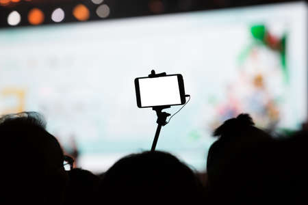 Hand with a smartphone records concert with blank white screenの写真素材