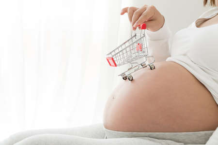 Pregnant women buy baby products and holding shopping cart in the white bedroom at home, Pregnancy shopping item for children conceptの写真素材