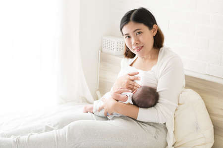 Asian mother holding her newborn baby boy and breastfeeding, Milk mother for child concept