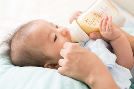 Hand of mother feeding baby with milk bottle