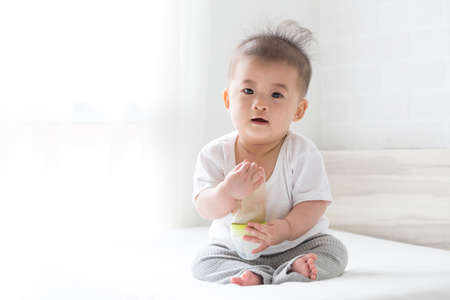 Asian baby boy holding a bottle milk on the bed at home