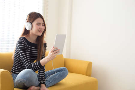 Young female student learning online or reading e-book with headphones and tablet in the room at...