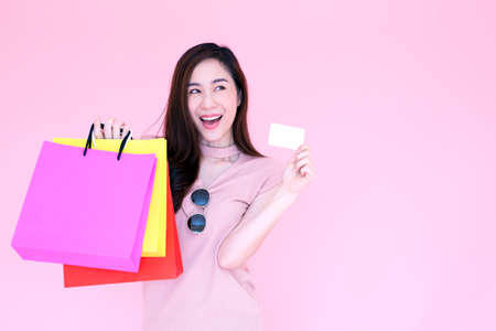 Beautiful asian women are shopping in the Valentine week, Happy pretty girl enjoys using a credit card and holding shopping bags in discount and sale festival isolated over pink backgroundの写真素材