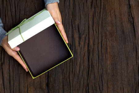 Top view of female hands holding gift box on wooden background and open the box with space to put...
