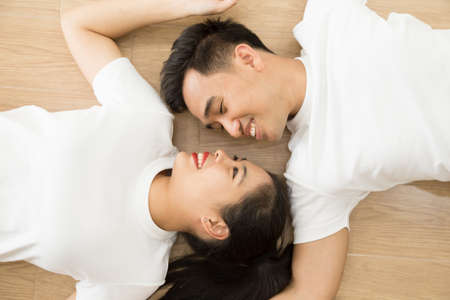Asian couple looking at each other and lying on the floor at home, True love and Pre-wedding...