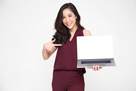 Young Asian businesswoman showing a laptop over white background and pointing finger to white screen of notebook with copy space for presenting application or website online or productsの写真素材