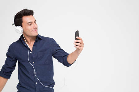 Handsome young Caucasian man listening music with headphones on smartphone, Teenager enjoying top chart music streaming service in website with his playlist on mobileの写真素材