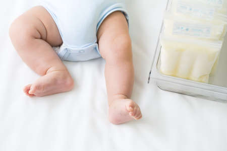 Breast milk frozen in storage bag and leg infant baby lying on white bedの写真素材