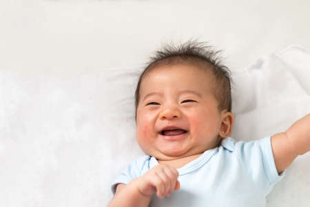 Happy little Asian baby smiling while lying on white bedの写真素材