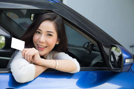 Asian woman holding personal accident insurance card and sitting in blue carの写真素材