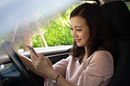 Asian woman using phone and sending a message behind the wheel, Female driving a car with using...