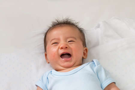 Happy little Asian baby smiling while lying on white bed