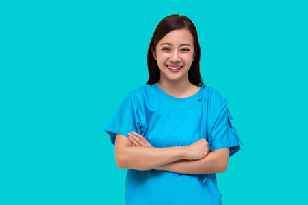 Asian smiling woman wearing patient suit with arms crossed isolated over blue backgroundの写真素材