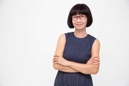 Portrait of asian senior woman with arms crossed isolated over white background, Elderly woman looking at camera conceptの写真素材