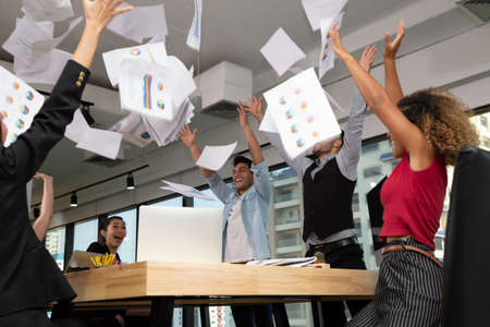 Group of business team throwing documents and triumph with arms up while celebrating success at...