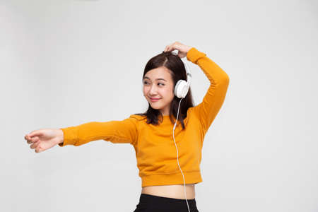 Beautiful young Asian woman with headphones listening to music in bright outfit enjoying the song melody isolated on white backgroundの写真素材