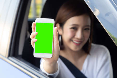 Asian woman driver sitting in the car and holding mobile phone with green screen backgroundの写真素材