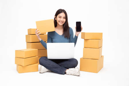 Young asian woman startup small business freelance holding parcel box, mobile phone and computer...