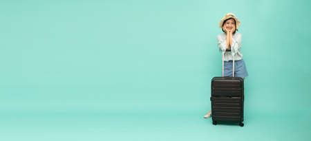 Asian woman traveler with suitcase on green color background, Happy young tourist with black baggage conceptの写真素材