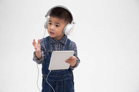 Portrait of a satisfied cute little kid holding tablet and listen music on application isolated over...
