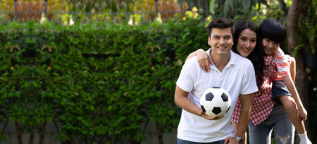Family playing football or soccer in green garden together their leisure time at summer holiday
