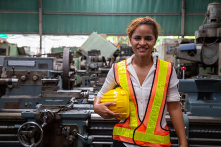 Female industrial engineer holding hard hat while standing in the heavy Industry manufacturing factoryの写真素材