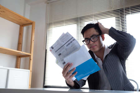 Sad confused and stressed of young Asian man holding bills letter of credit card debt