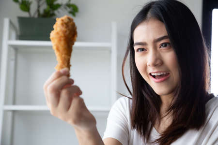 Young Asian woman eating chicken in the room at home and feeling happiness delightの写真素材