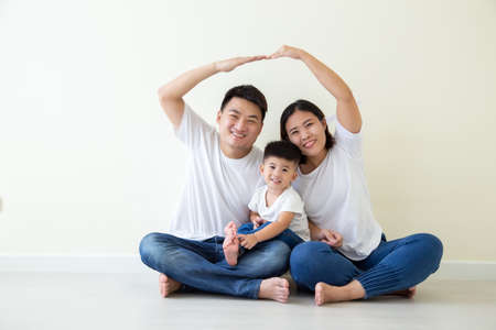 Dad and mom making roof figure home with hands arms over heads, Asian Family with son sitting on floor in the room, New building residential house purchase apartment conceptの写真素材