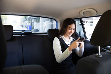 Asian teenager woman using a smartphone in back seat of car, Passengers use an app to order a ride and Peer-to-peer ride sharing conceptの写真素材