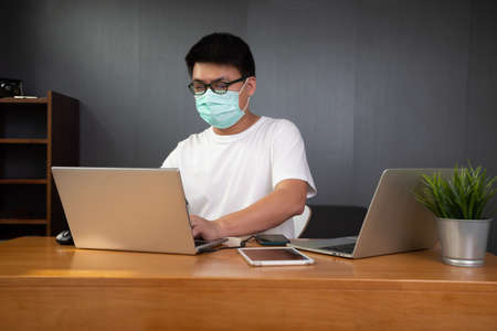 Asian man it support working with computer laptop to remote desktop and wearing protective medical...