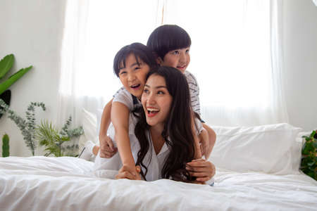 Happiness of Asian family with mom and son and daughter hug mother on white bed in bedroom, Feeling happy and family relationship conceptの写真素材