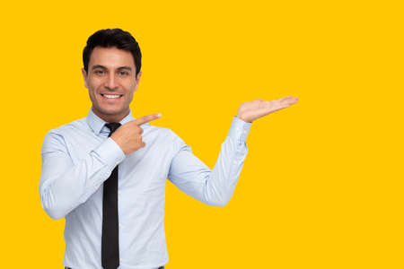 Businessman smiling and pointing to empty copy space isolated on yellow backgroundの写真素材