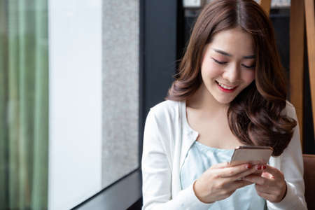 Charming Asian woman smile reading good news on mobile phone during rest in coffee shopの写真素材