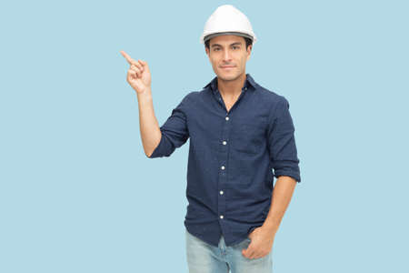 Handsome man industrial engineer wearing a white hard helmet and pointing finger towards something...