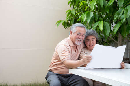 Happy Asian senior mature couple reading newspaper or magazine at front garden homeの写真素材