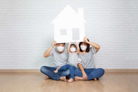 Asian family wearing protective mask for prevent virus and holding paper home, New house and real estate concept