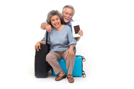 Asian senior couple sitting on travel bag isolated over white background, Travelers and tourism conceptの写真素材
